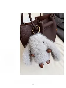 Detail of grey plush rabbit charm with gold metal clasp on brown leather bucket bag