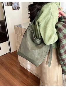 Detail of olive green suede hobo bag with wide strap worn over a cozy green sweater