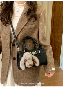Detail of black pebble leather crossbody bag with silver buckle and plush rabbit charm