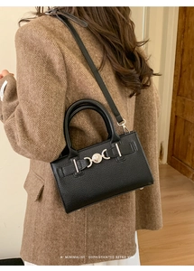 Detail showing a black retro crossbody bag with silver heart buckle on a model's side