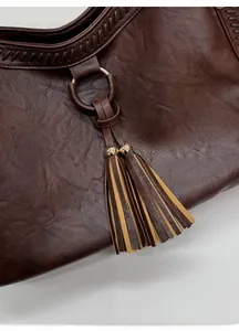 Close-up of brown textured leather bag with gold rings and decorative bicolor tassels