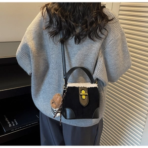 Close-up of black suede bucket bag with white fleece trim and gold metal swivel lock