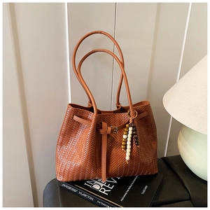 Gros plan sur un cabas tissé marron avec sangle en cuir et breloque en perles