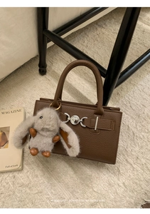Detail of brown litchi pattern tote bag featuring a plush bunny charm and silver metal clasp