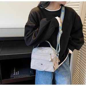 Detail of light gray multi-zipper crossbody bag with colorful patterned wide strap