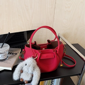 Chic red drawstring bucket bag with cute plush bunny charm on a minimalist desk setup