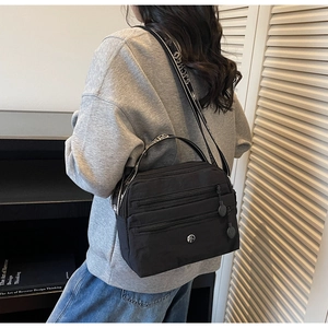Detail showing the black nylon crossbody bag with three zipper compartments and logo plaque