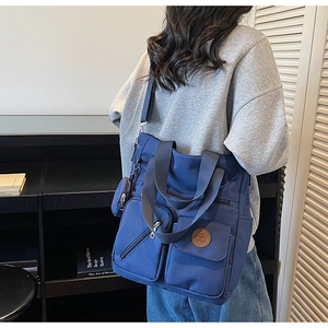 Deep blue nylon tote bag with multiple pockets shown on model in a casual indoor setting