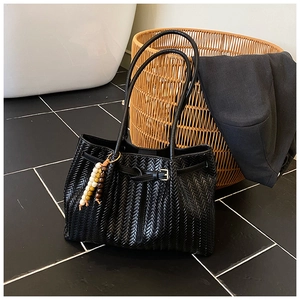 Détail du cabas tressé noir avec boucle de ceinture vintage et breloque en perles de bois