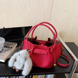 Detail of fuchsia lychee leather bucket bag with a grey plush rabbit charm on desk