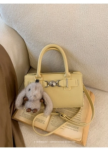 Close-up of yellow lychee pattern bag with silver buckle and plush bunny charm on a book