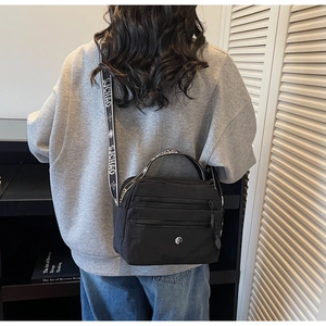Model view of black nylon crossbody bag with multi-zipper layers and printed strap