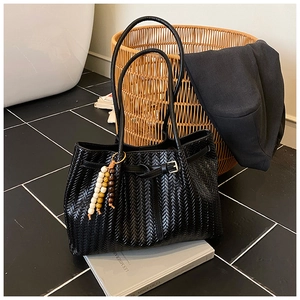 Détail d'un sac cabas noir tissé avec texture vintage et charmant pendentif en perles