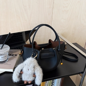Close-up of black lychee grain leather bucket bag with a plush rabbit charm and gold hardware