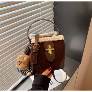 Detail of a brown suede bucket bag featuring faux shearling trim and a cute bear charm