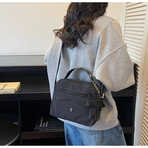 Detail of black nylon crossbody bag with three zipper compartments and wide strap