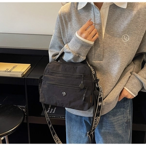 Detail of black nylon crossbody bag with multi-zipper pockets and letter print strap