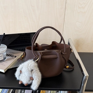 Detailed macro view of brown litchi grain leather bucket bag with plush bunny keychain