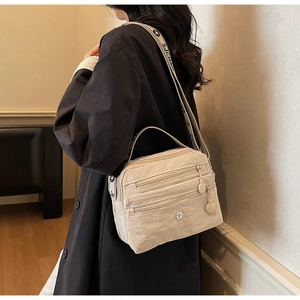Detailed side view of beige nylon crossbody bag with multi-layer zippers and woven strap