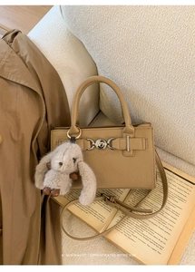 Close-up of tan lychee pattern leather handbag with vintage silver buckle and plush bunny charm