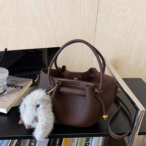 Close-up of deep brown lychee grain leather bucket bag with a plush rabbit charm