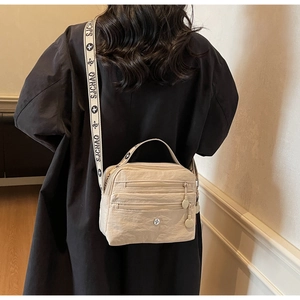 Detail of a beige crossbody bag featuring multi-layer zippers and floral woven strap