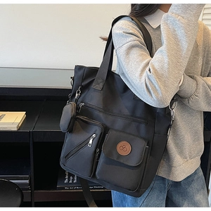 Detail view of black nylon tote bag featuring external pockets and a small round pouch