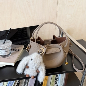 Detail view of lychee grain bucket bag with plush bunny charm on office desk