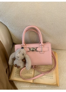 Detail view of pink lychee leather handbag with silver lock and plush bunny charm