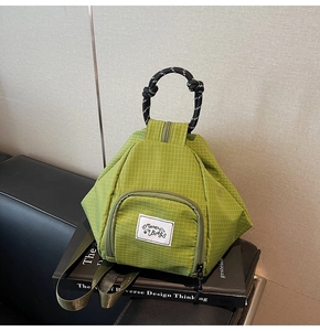 Detail of green plaid bag featuring woven rope handles and a front zipper pocket