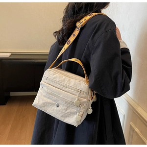 Detail of beige nylon crossbody bag with multi-layer zippers and yellow patterned strap