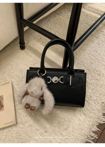 Detail of black lychee leather handbag with silver heart buckle and plush bunny charm