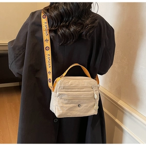 Detail of beige nylon crossbody bag featuring stylish patterned jacquard strap and dual zippers