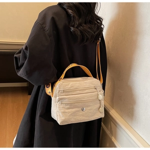 Detail of beige nylon crossbody bag featuring three-layer zipper pockets and jacquard strap