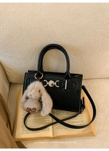 Close-up of black litchi grain leather bag with metal buckle and rabbit plush charm