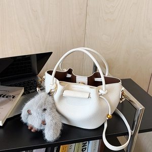 Detail of white litchi pattern bucket bag with grey plush bunny charm on black desk