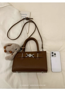 Detail view of retro brown textured leather crossbody bag with metal buckle and plush charm