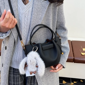 Detail of black lychee leather bucket bag with white plush ball charm on a model