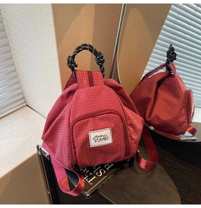 Detail of red checkered canvas backpack with woven handle and Muran logo on a vintage table