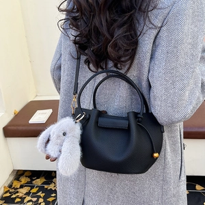 Detail of black pebbled leather bucket bag with a plush bunny charm on a wool coat