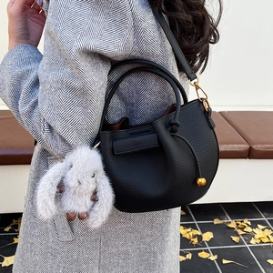 Close-up of black lychee grain leather bucket bag with golden hardware and plush bunny charm