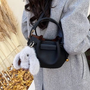 Detail of black lychee grain leather bucket bag featuring a cute grey plush bunny charm
