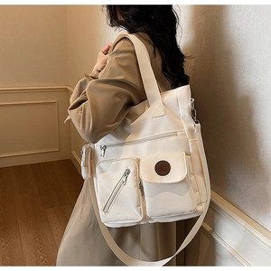 Detail view of a large cream tote bag with dual handles and multiple functional zippers