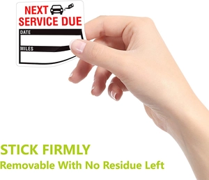 Close-up of hand peeling a waterproof car oil change reminder sticker with date and mileage