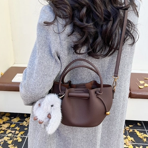 Outdoor shot of dark brown pebbled leather bucket bag with white bunny charm