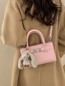 Pink faux leather shoulder bag with plush bunny charm on camel wool coat
