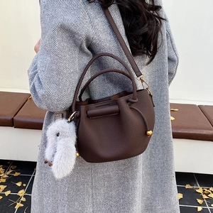 Brown litchi grain leather bucket bag with plush rabbit charm worn over a grey coat