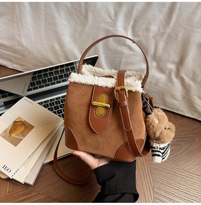 Detail of suede bucket bag featuring white plush trim, metal turn-lock and bear charm