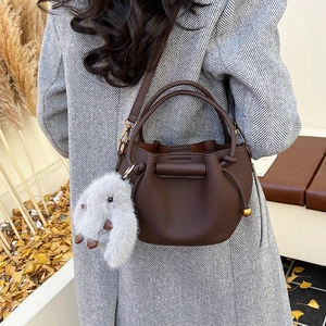 Detail of dark brown leather bucket bag with gold hardware and plush rabbit charm