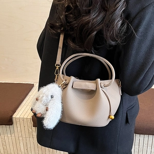 Detail of greige pebbled leather bucket bag with plush rabbit charm and shoulder strap